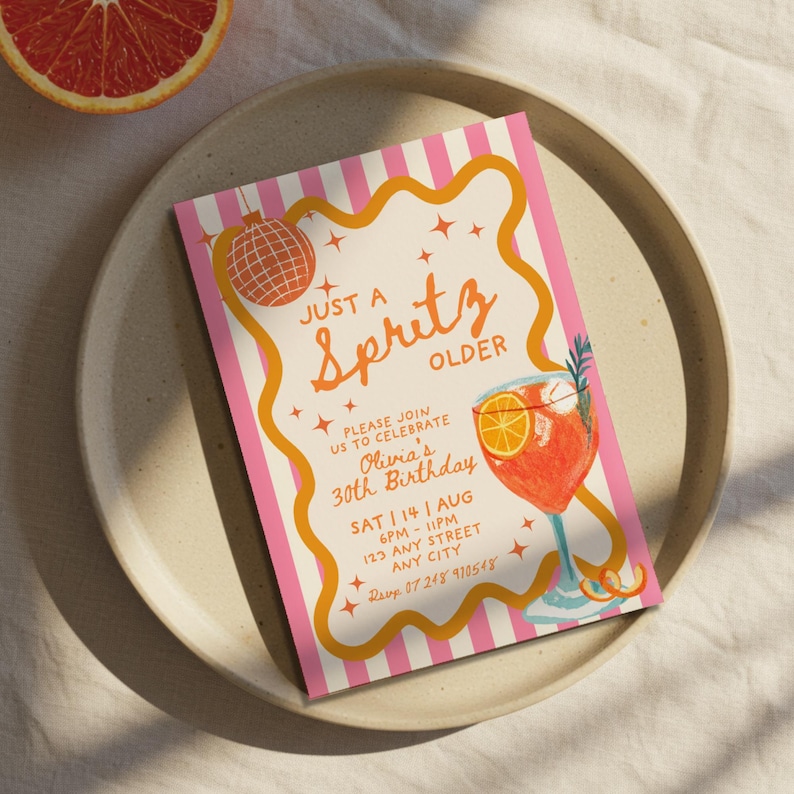 Op de afbeelding: Een roze en wit gestreepte uitnodiging met de tekst "Just a Spritz Older" in oranje script. De uitnodiging bevat details voor Olivia's 30e verjaardag, met een cocktailillustratie en een discobal-afbeelding.