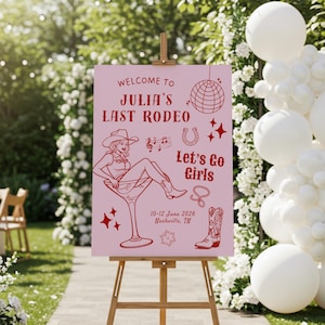 Puede incluir: Un letrero rosa sobre un caballete de madera con el texto "WELCOME TO JULIA'S LAST RODEO" y "Let's Go Girls". El letrero presenta una ilustración de vaquera en una copa de martini, una herradura, notas musicales y una bota de vaquero.