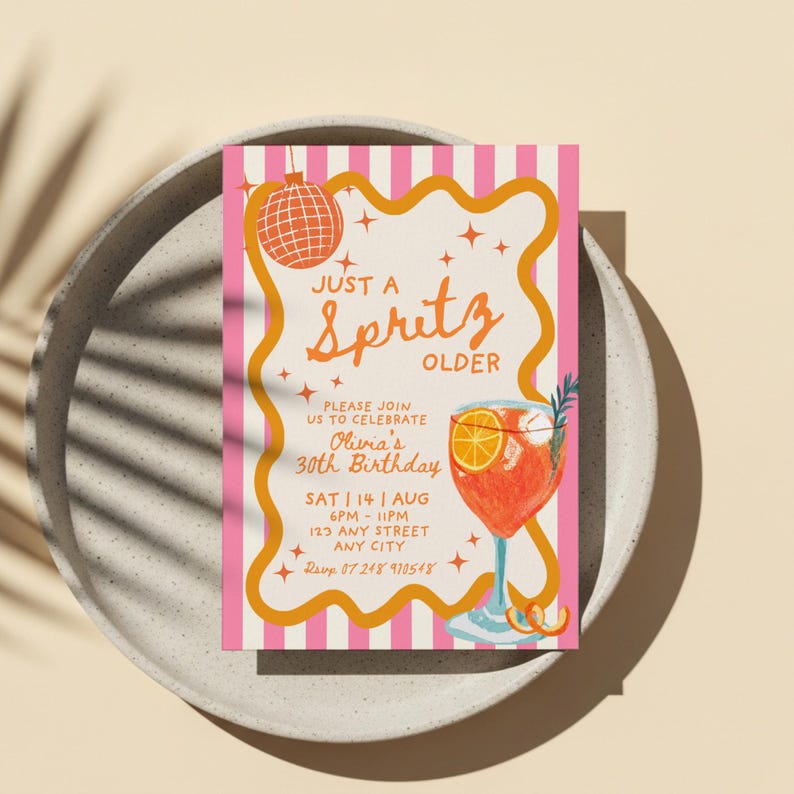 Op de afbeelding: Een uitnodiging voor een feestje met een roze en witte gestreepte achtergrond. De uitnodiging bevat de woorden "Just a Spritz Older" in oranje schrift, samen met een cocktailillustratie. De uitnodiging is voor Olivia's 30e verjaardag.