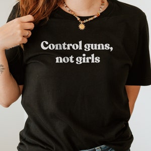 May include: Black t-shirt with the text "Control guns, not girls" printed in white.