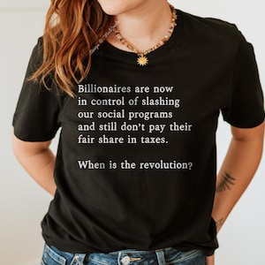 May include: Black t-shirt with white text that reads "Billionaires are now in control of slashing our social programs and still don't pay their fair share in taxes. When is the revolution?"