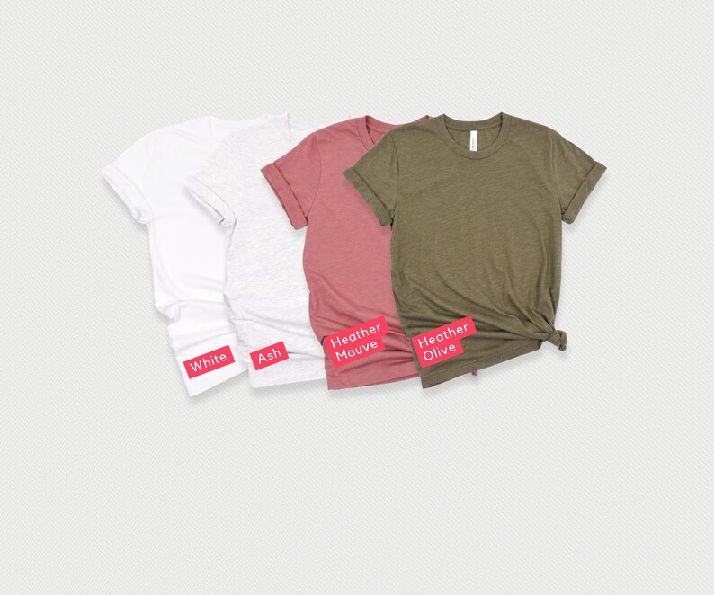 May include: Four t-shirts in different colors: white, ash, heather mauve, and heather olive. The shirts are folded and laid out on a white background.