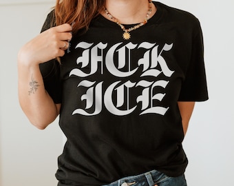 May include: Black t-shirt with the text "F*CK ICE" in large, white, gothic-style lettering. The shirt is a crew neck and appears to be made of a soft material. The shirt is being worn by a person.