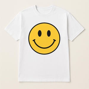 Könnte beinhalten: Weißes T-Shirt mit einem großen gelben Smiley-Gesicht in der Mitte. Das Smiley-Gesicht hat schwarze Augen und eine schwarze Umrandung. Das T-Shirt hat kurze Ärmel und einen Rundhalsausschnitt.