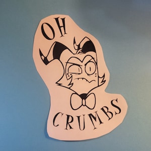 Pode incluir: Um adesivo branco com uma ilustração de desenho animado em preto e branco de um personagem com chifres e uma gravata borboleta. O texto "OH CRUMBS" está escrito abaixo do personagem.