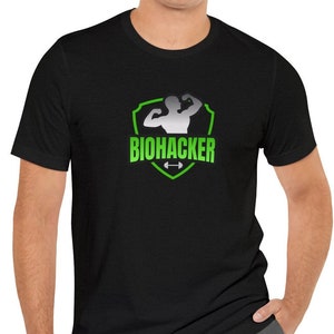 Może przedstawiać: Czarny T-shirt z zielonym i srebrnym nadrukiem tarczy z napisem "BIOHACKER".