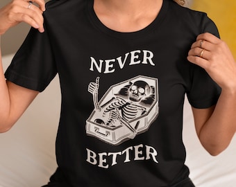 Puede incluir: Camiseta negra con un gráfico blanco de un esqueleto en un ataúd con el texto "NEVER BETTER".