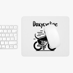 May include: A black and white mouse mat with a black silhouette of a dog riding a bicycle. The text "Doxycycline" is written in black above the dog.