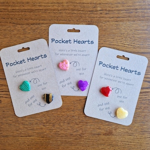 May include: Three brown cards with the text "Pocket Hearts" and the phrase "Here's a little heart for whenever we're apart". Each card has two small heart-shaped charms with different patterns and colours. The text "one for you" and "and one for me" is written on each card.