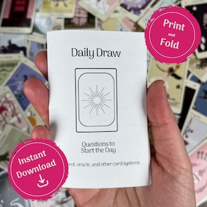 May include: A white booklet titled "Daily Draw" with a sunburst design inside a rectangular frame. The text "Questions to Start the Day" is below the design. Pink circles with the text "Print and Fold" and "Instant Download" are also visible.