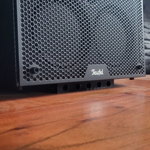 Peut inclure: Un haut-parleur noir avec une grille hexagonale et le mot "Teufel" imprimé sur le devant.