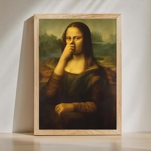 May include: A framed print of the Mona Lisa with a humorous twist. The iconic figure is depicted with a finger touching her nose. The artwork is set against a landscape background and framed in a light-colored wooden frame.