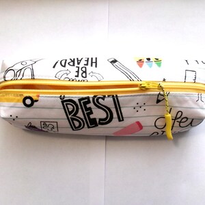 May include: A white pencil case with a yellow zipper and a yellow pull tab. The case is decorated with a black and white doodle pattern that includes the words "BE HEARD", "BEST", and "of course".