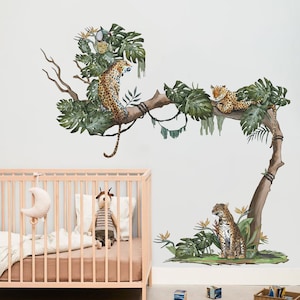 May include: Three leopard print animal stickers on a white wall. The leopards are on a branch with green leaves. One leopard is sitting on the branch, one is lying down, and one is standing on the ground.