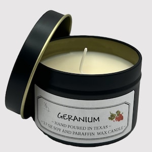 Könnte beinhalten: Eine schwarze Blechkerze mit goldenem Deckel. Die Kerze ist mit "GERANIUM ~HAND POURED IN TEXAS~ -3.7 OZ SOY AND PARAFFIN WAX CANDLE~" beschriftet.