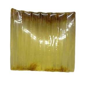 Könnte beinhalten: Ein rechteckiger Seifenblock in transluzentem, bernsteingelbem Farbton. Die Seife hat eine strukturierte Oberfläche mit vertikalen Linien und einem etwas dunkleren Braunton an der Ober- und Unterseite. Die Seife scheint handgemacht zu sein.