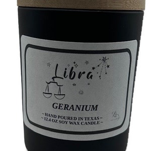 Könnte beinhalten: Schwarzes Kerzengefäß mit einem Holzdeckel. Das Etikett zeigt "Libra" mit einer Sternenkonstellation und "Geranium" mit dem Text "Hand poured in Texas - 12.4 oz Soy Wax Candle".