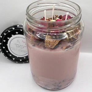 Könnte beinhalten: Eine rosa Sojawachskerze in einem Glasgefäß mit einem schwarz-weißen Deckel. Die Kerze ist mit getrockneten Blumen verziert und hat drei Dochte. Das Etikett auf dem Glas lautet "Cherry Blossom & Gardenia Rose Tincs 33.5 oz Soy Handmade Candle Hand Poured in Texas."