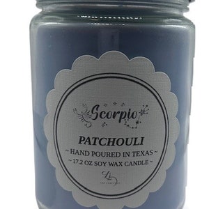 Könnte beinhalten: Eine blaue Glaskerze in einem Glas mit einem silbernen Etikett, auf dem "Scorpio Patchouli - Hand Poured in Texas - 17.2 oz Soy Wax Candle" steht.