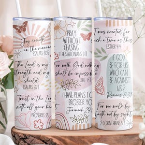 Puede incluir: Tres vasos aislados blancos con citas inspiradoras y dise&ntilde;os florales y de mariposas. Cada vaso tiene una pajita y presenta una cita diferente de la Biblia en una fuente manuscrita. Los vasos est&aacute;n decorados con colores pastel.