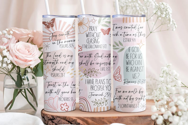 Puede incluir: Tres vasos aislados blancos con citas inspiradoras y dise&ntilde;os florales y de mariposas. Cada vaso tiene una pajita y presenta una cita diferente de la Biblia en una fuente manuscrita. Los vasos est&aacute;n decorados con colores pastel.