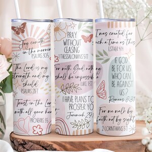Puede incluir: Tres vasos aislados blancos con citas inspiradoras y dise&ntilde;os florales. Cada vaso presenta una cita diferente en escritura negra, junto con mariposas y rayos de sol decorativos. Los vasos se exhiben sobre una superficie de madera.