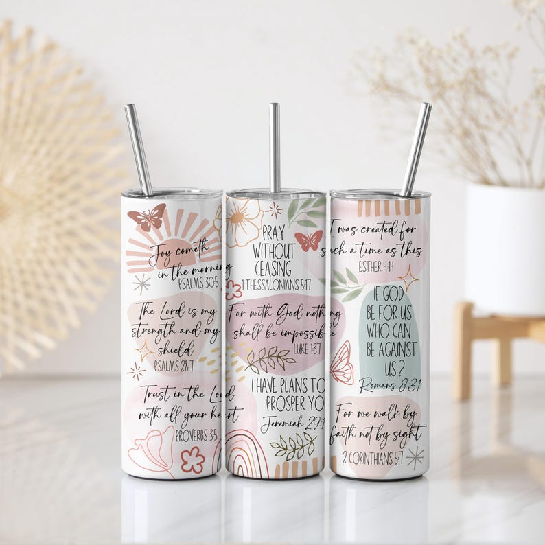 Puede incluir: Tres vasos aislados de acero inoxidable con tapas y pajitas. Cada vaso presenta un dise&ntilde;o &uacute;nico con citas inspiradoras, ilustraciones florales y de mariposas, y referencias b&iacute;blicas. Los vasos son blancos con detalles en rosa y beige.