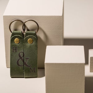 May include: Two green leather keychains with metal rings. The keychains have the letters "H & M" engraved on them.