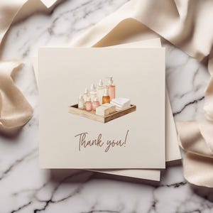 May include: A thank you card with a watercolor illustration of a wooden tray filled with various bottles of bath and body products, including soaps and lotions. The text "Thank you!" is written in brown cursive.