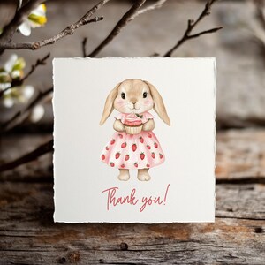 K&ouml;nnte beinhalten: Aquarellillustration eines H&auml;schens, das einen Cupcake h&auml;lt und ein rosa Kleid mit Erdbeerakzenten tr&auml;gt. Die Karte tr&auml;gt die Aufschrift "Thank you!" in einer Schreibschrift. Das H&auml;schen hat lange Ohren und einen s&uuml;&szlig;en Ausdruck.