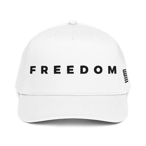 May include: White baseball cap with the word "FREEDOM" printed in black across the front. The cap has a curved brim and a small design on the side. A stylish accessory for everyday wear.