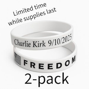 Puede incluir: Dos pulseras de goma blancas apiladas. La pulsera superior tiene el texto "Charlie Kirk 9/10/2025". La pulsera inferior tiene una bandera estadounidense y la palabra "FREEDOM". El texto "2-pack" está debajo. El texto "Limited time while supplies last" está arriba.