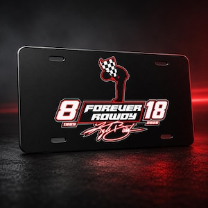 May include: Black license plate featuring the number 8 and 18 in white and red, with the text "FOREVER ROWDY" and a checkered flag graphic. The years 1985 and 2026 are also displayed. The plate has a glossy finish.