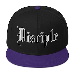 Puede incluir: Gorra de béisbol negra y morada con la palabra "Disciple" bordada en letras góticas blancas. La gorra tiene una visera y un botón morados, y una corona negra.
