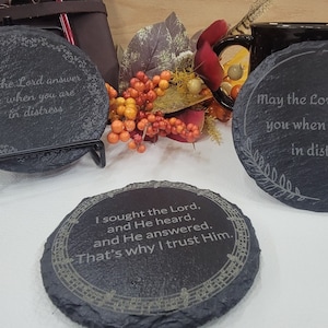 May include: Three black slate coasters with inspirational quotes and decorative borders. The quotes are: "May the Lord answer you when you are in distress", "May the Lord answer you when you are in distress Psalm 20:1", and "I sought the Lord, and He heard, and He answered. That's why I trust Him."