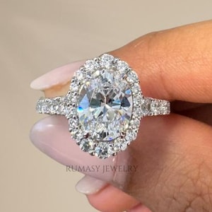 May include: A silver engagement ring with a large oval-shaped diamond surrounded by a halo of smaller diamonds. The ring has a pave setting with smaller diamonds lining the band.