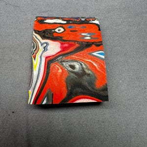 May include: A rectangular piece of material with a vibrant, swirled pattern. The design features bold red, black, white, and yellow colours, creating a dynamic and abstract visual effect. The material appears to be solid and polished.