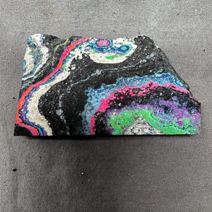 May include: A piece of rock with a black base and colorful swirls of white, pink, blue, green, and purple. The rock has a rough, textured surface and an irregular shape. The colors create a vibrant, abstract pattern.