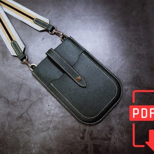 May include: A dark green leather phone case with a white and black striped strap. The case has a flap with a snap closure and a small pocket on the front. The case is designed to hold a smartphone.