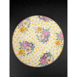 Op de afbeelding: Een ronde, witte plaat met een gele stippenpatroon en bloemstukken. De bloemen zijn in tinten roze, geel en paars. De plaat heeft een gouden rand.
