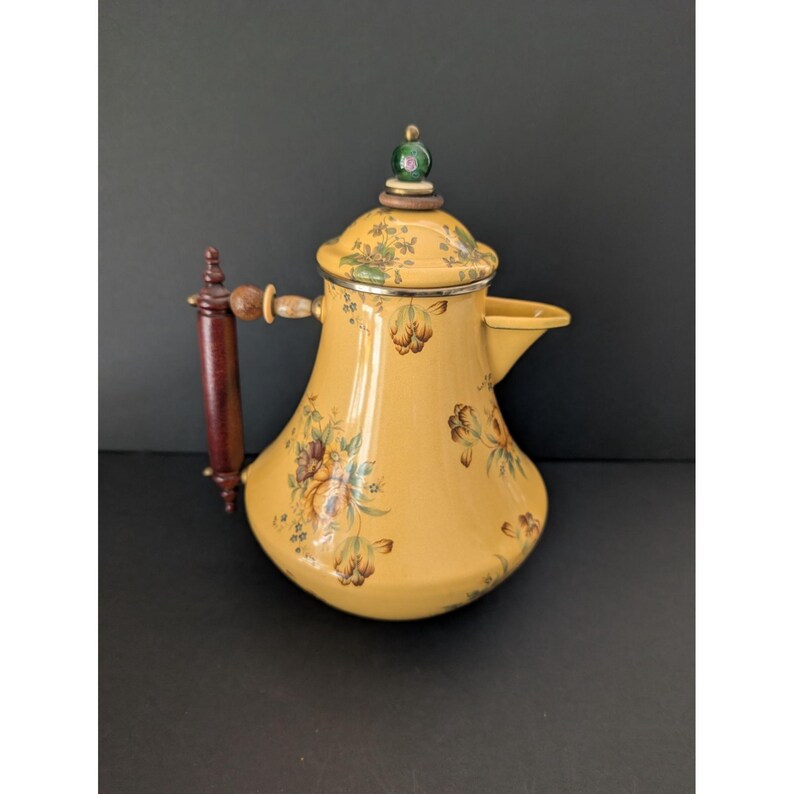 May include: Yellow vintage teapot with floral design. The teapot has a dark brown wooden handle and a lid with a green and gold finial. The teapot is decorated with brown, green, and yellow flowers.