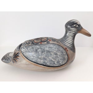 Może przedstawiać: Ręcznie malowana ceramiczna figurka kaczki z szarymi, białymi, brązowymi i czerwonymi akcentami. Kaczka leży z głową odwróconą na bok.