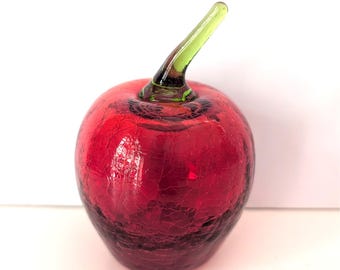 May include: A decorative glass apple with a crackle finish in shades of red. The apple has a green stem. The glass apple is a unique home decor item.