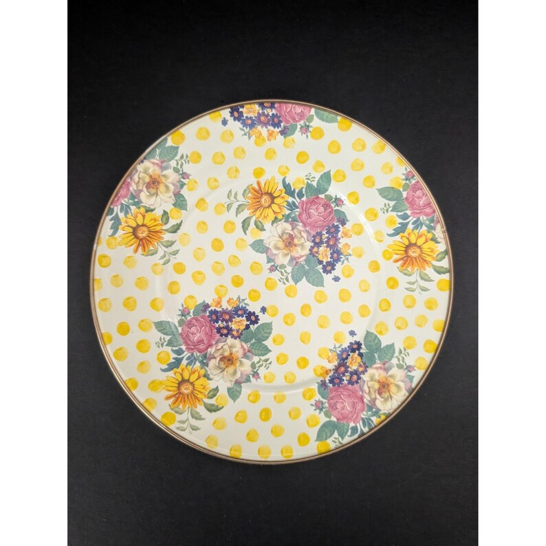 Op de afbeelding: Een ronde, decoratieve plaat met een geel stippenpatroon en bloemboeketten. De boeketten bevatten roze rozen, gele zonnebloemen en paarse bloemen. De plaat heeft een gouden rand en staat tegen een zwarte achtergrond.