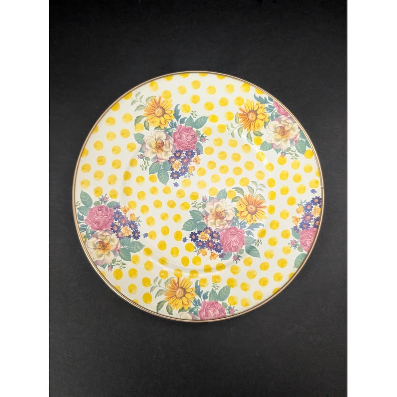 Op de afbeelding: Een ronde, decoratieve plaat met een gele stippenpatroon en bloemstukken. De bloemen zijn in tinten roze, geel en paars, met groene bladeren. De plaat heeft een gouden rand.