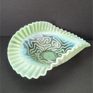 May include: A green iridescent glass bowl with a ruffled edge and a swirl design. The bowl is made of opalescent glass and has a vintage look.