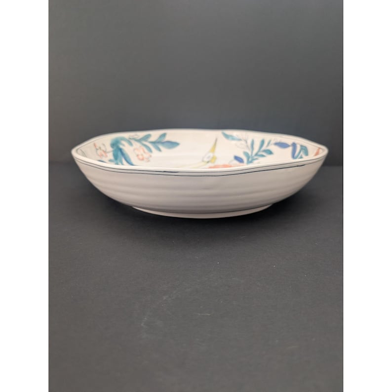 May include: A white ceramic bowl with a floral design. The bowl has a slightly irregular shape and a blue line around the rim. The floral pattern includes blue and green leaves and pink and yellow flowers.