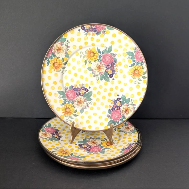 Op de afbeelding: Set van vier decoratieve borden. De borden hebben een witte achtergrond met gele stippen en bloemstukken van roze, gele en paarse bloemen. Elk bord heeft een gouden rand.