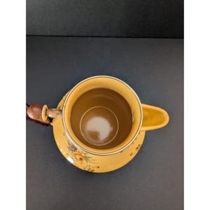 May include: Yellow ceramic teacup and saucer set with floral designs. The teacup has a handle and a brown interior. The saucer is round and has a matching floral pattern. The set is placed on a dark surface.