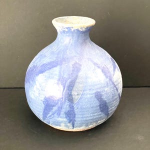 Könnte beinhalten: Eine runde Keramikvase mit engem Hals und ausgestelltem Rand. Die Oberfläche weist eine texturierte, gesprenkelte Glasur in hellen und dunklen Blautönen auf, mit sichtbaren Pinselstrichmustern und einem matten Finish, das den Ton durchscheinen lässt.